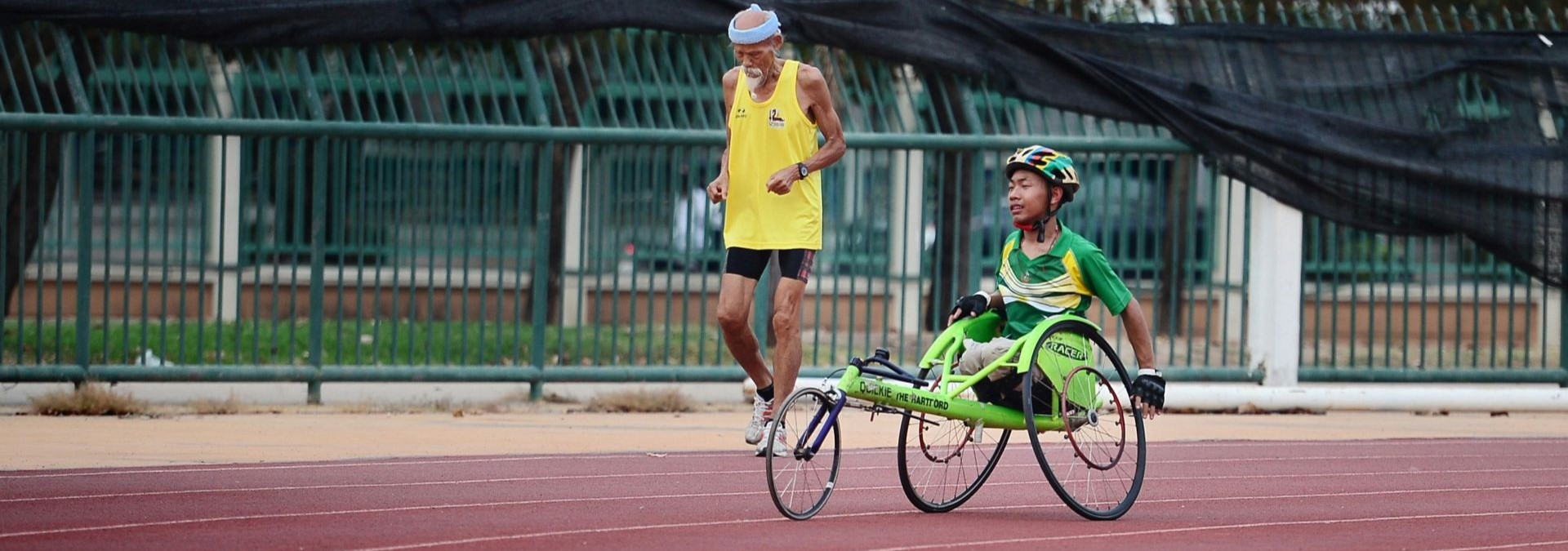 Ein junge im Rollstuhl und ein älterer Mann treiben zusammen auf einer Sprintstrecke sport
