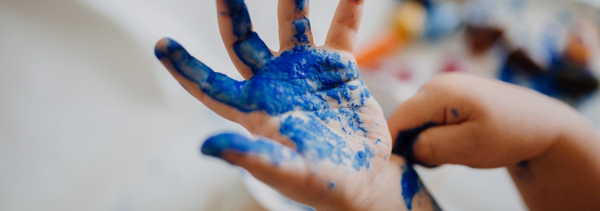 eine kinderhand die mit blauer Malfarbe angemalt wurde, der hintergrund ist verschommen